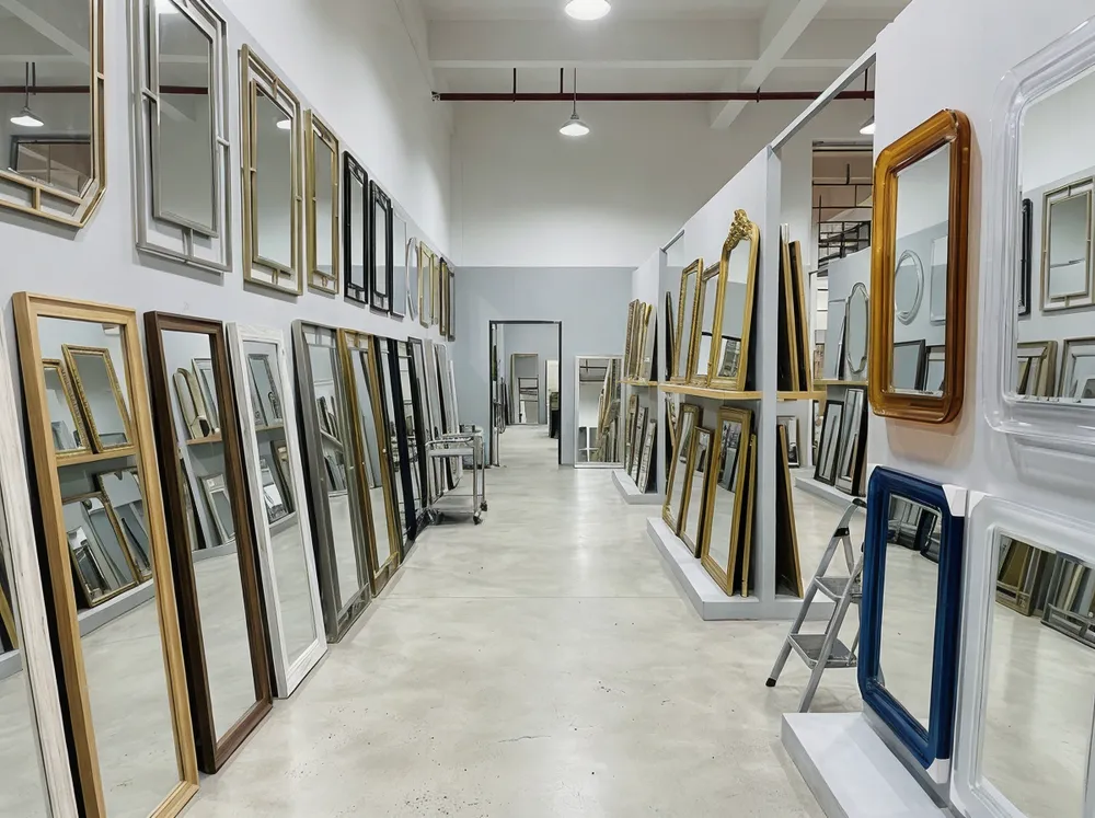 Variety of decor mirror frame materials including wood, metal, acrylic, and gold finishes displayed in factory showroom