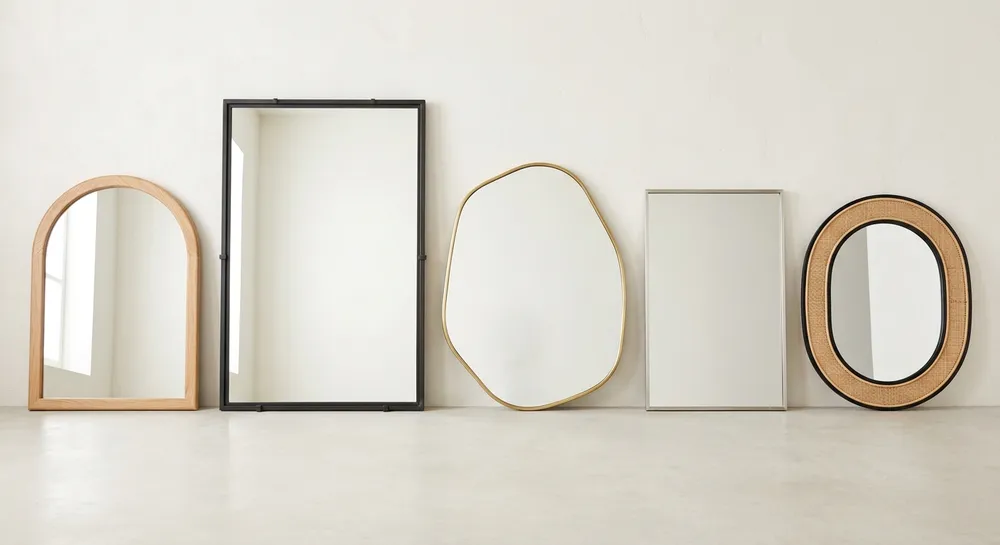 Assortment of 2026 living room mirror styles including arched, oversized, and mixed-material frames displayed against a neutral wall