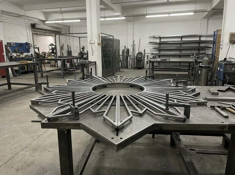 CNC-machined jig holding sunburst mirror frame segments in precise 30-degree alignment before welding