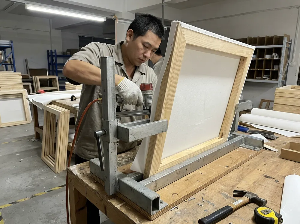 Canvas being stretched and stapled onto kiln-dried pine stretcher bars on a squaring jig