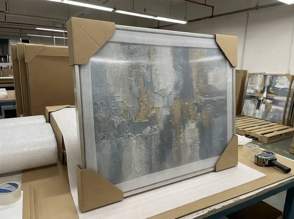 Protective packaging layers for textured abstract wall art showing foam separator, corner protectors, and rigid face shield